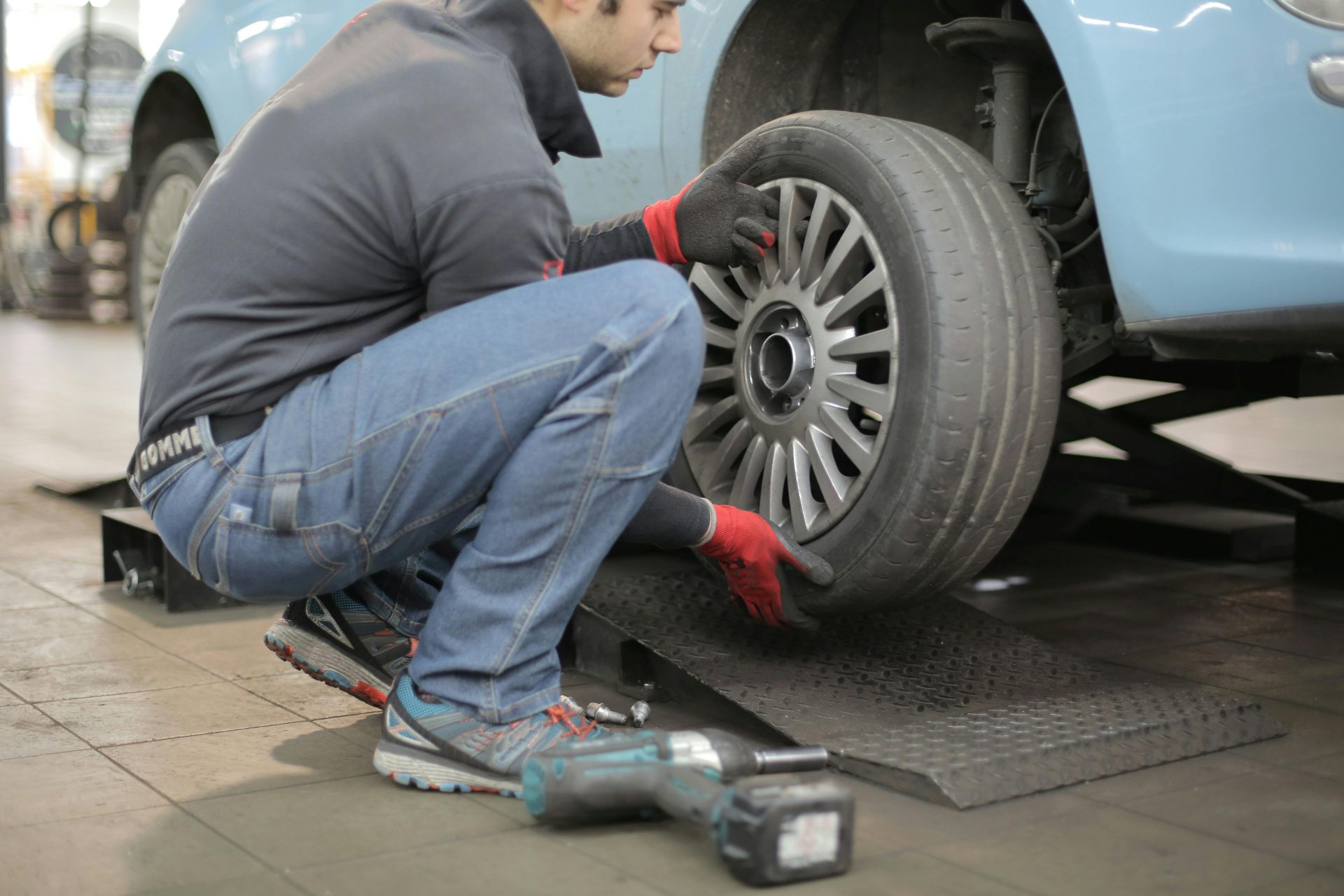 Mecánico cambiando un neumático de coche en el interior, utilizando herramientas para el mantenimiento del vehículo.