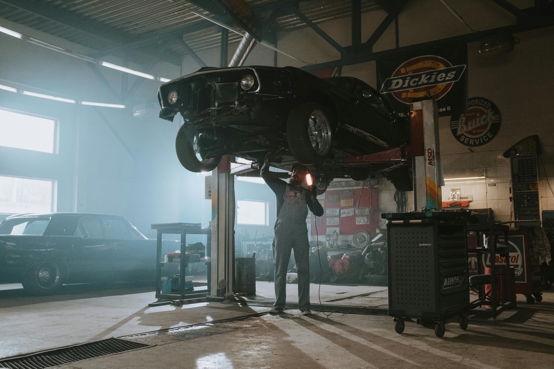 Mecánico masculino utiliza una luz para inspeccionar un automóvil clásico levantado en un garaje de automóviles.