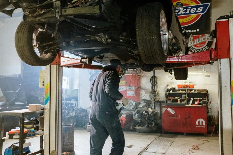 Mecánico reparando un vehículo en un taller concurrido con varias herramientas automotrices.